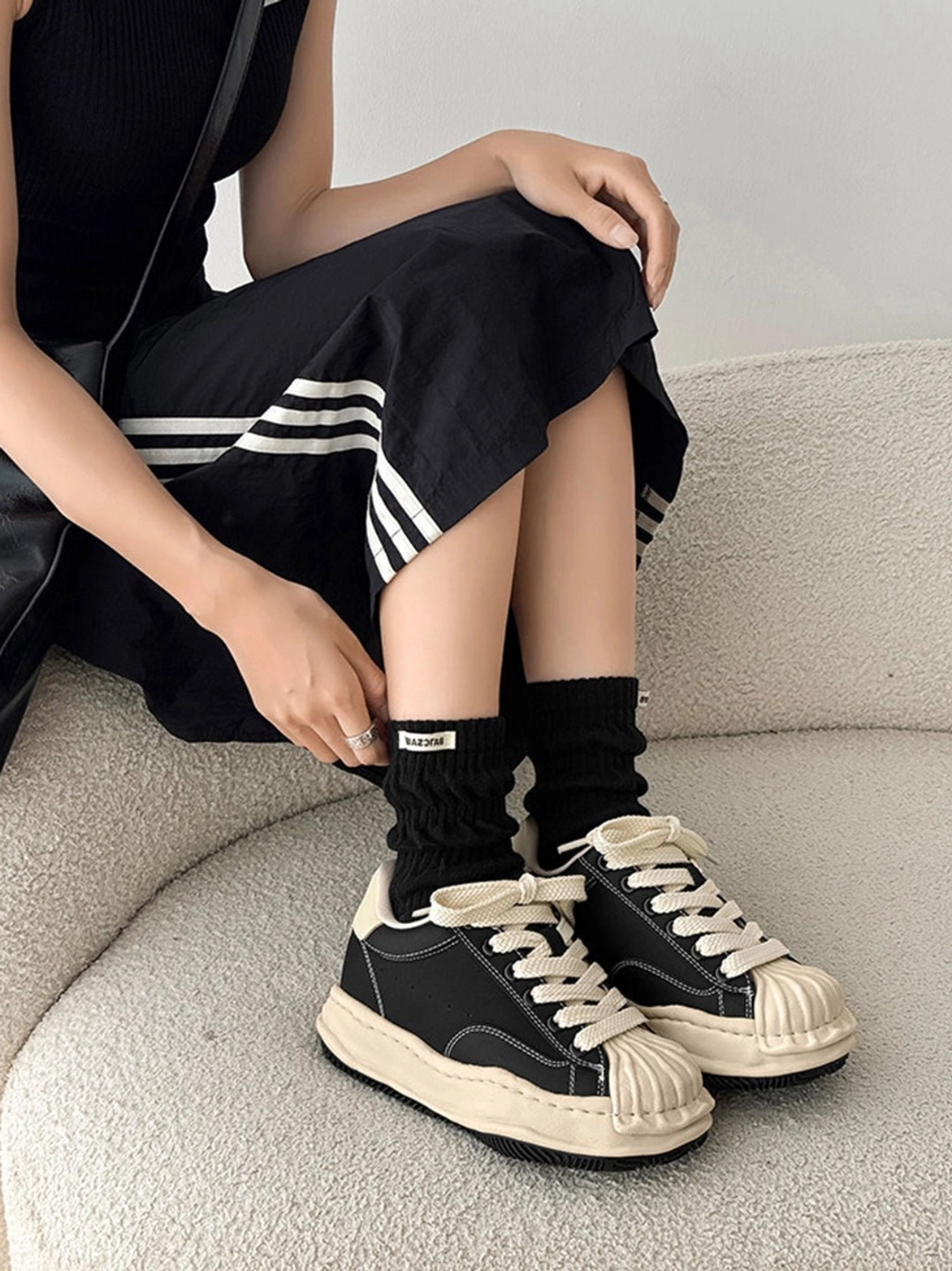Pair of black and cream shell-toe platform sneakers styled with slouch socks and striped midi skirt
