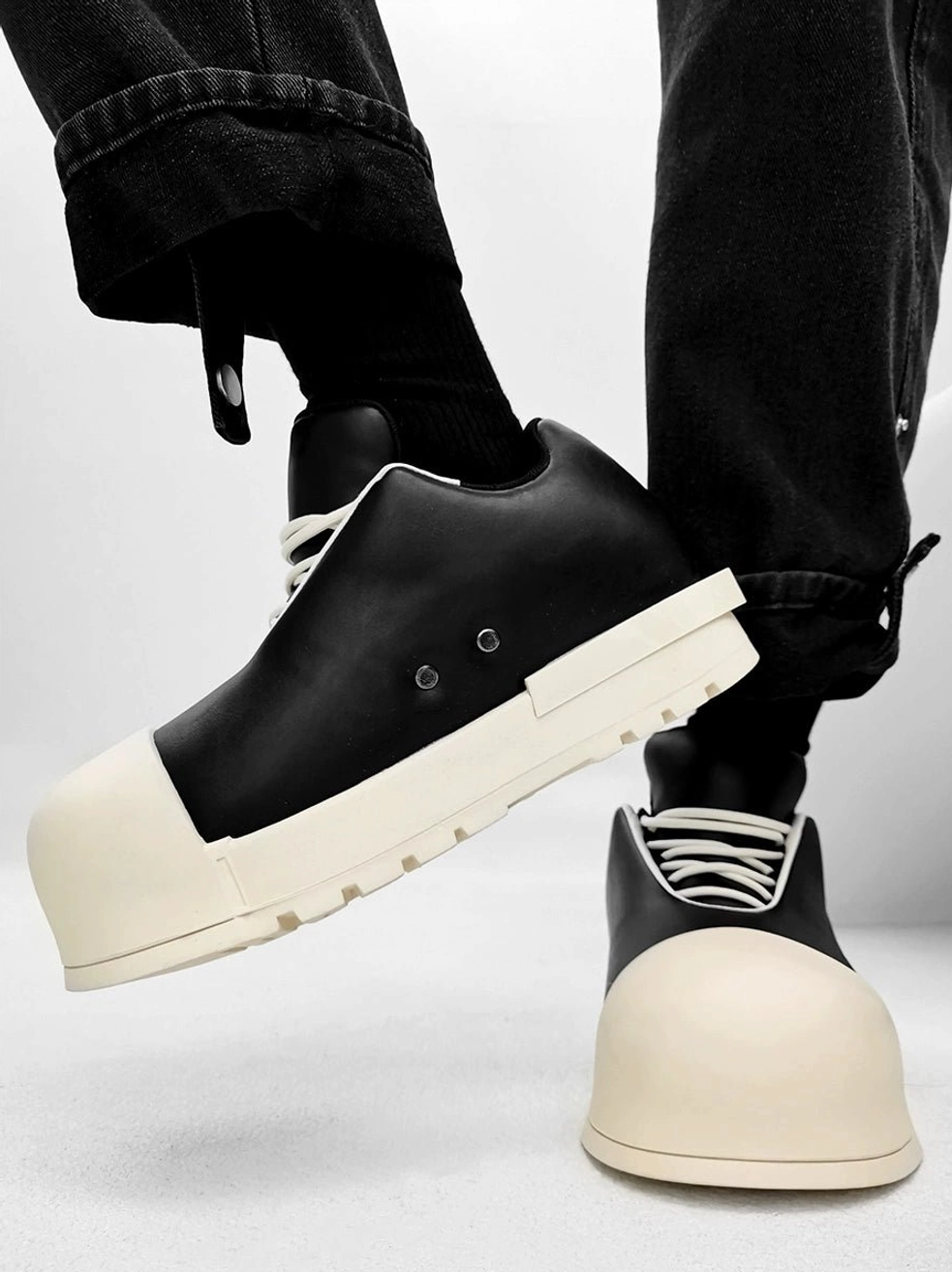 Two-tone black and cream oversized platform sneakers shown from a low angle with chunky sole, contrast laces, and metal heel details
