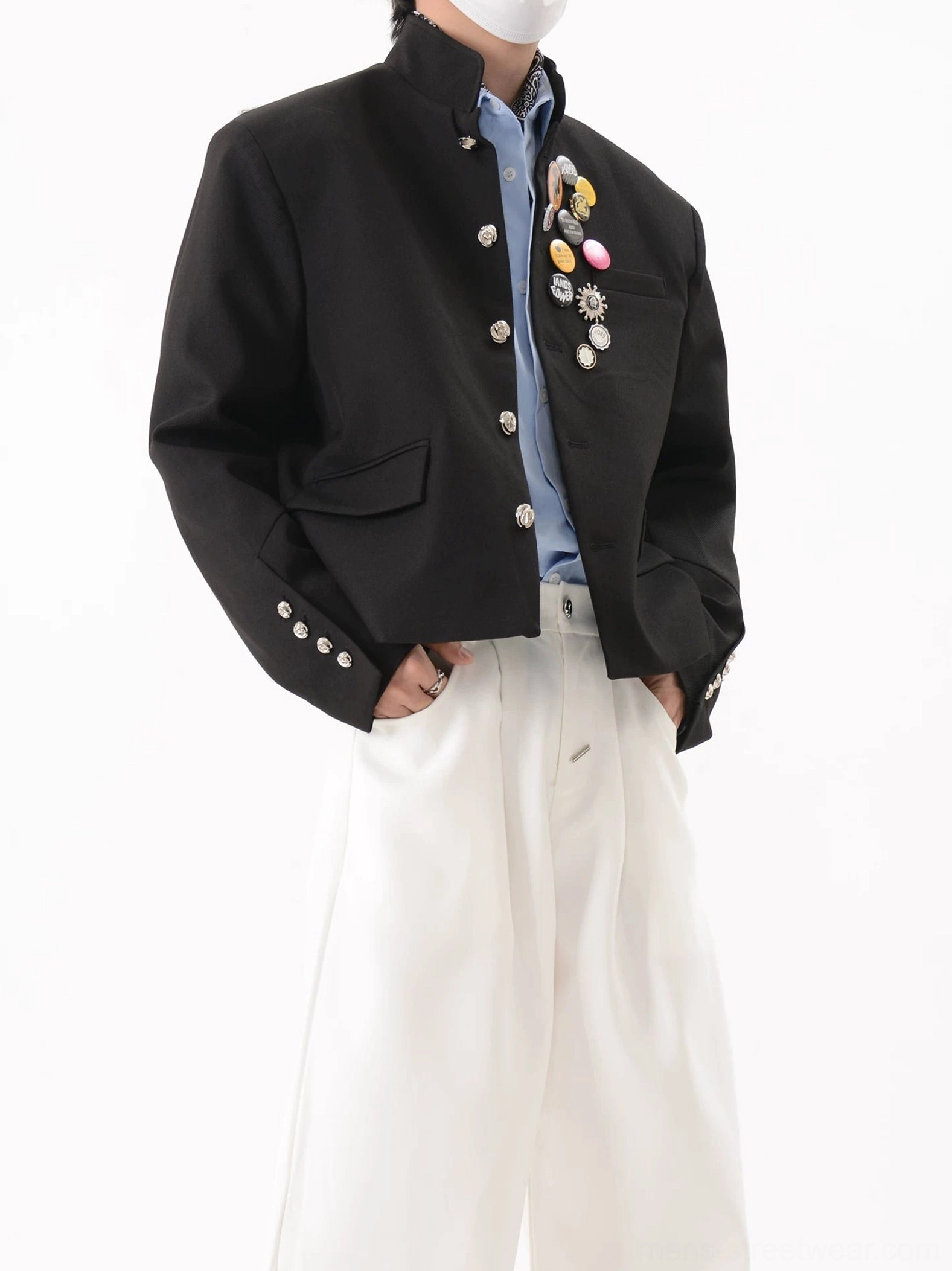 Close-up front view of black crest pin cropped blazer with polished silver buttons buttoned cuffs and layered blue shirt styling