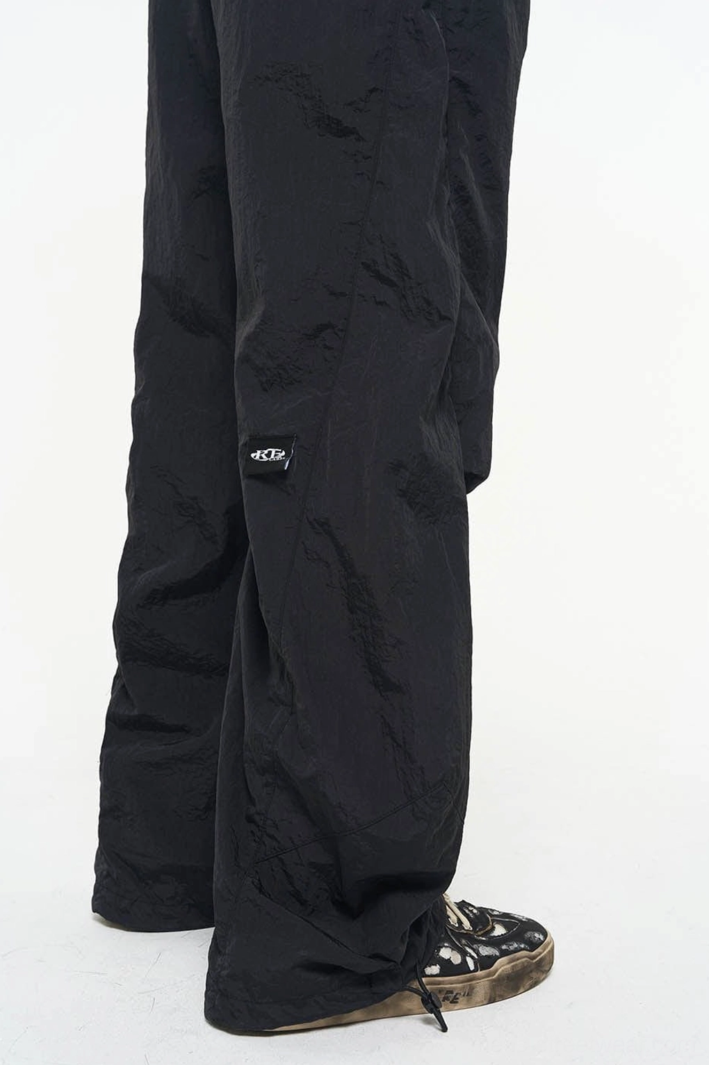 Side lower-leg detail of black nylon wide-leg track pants with adjustable drawstring hem and textured fabric