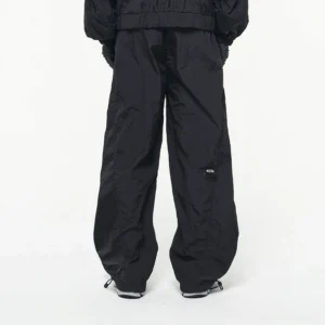 Back view of black crinkled nylon wide-leg track pants with loose silhouette and adjustable ankle drawcords