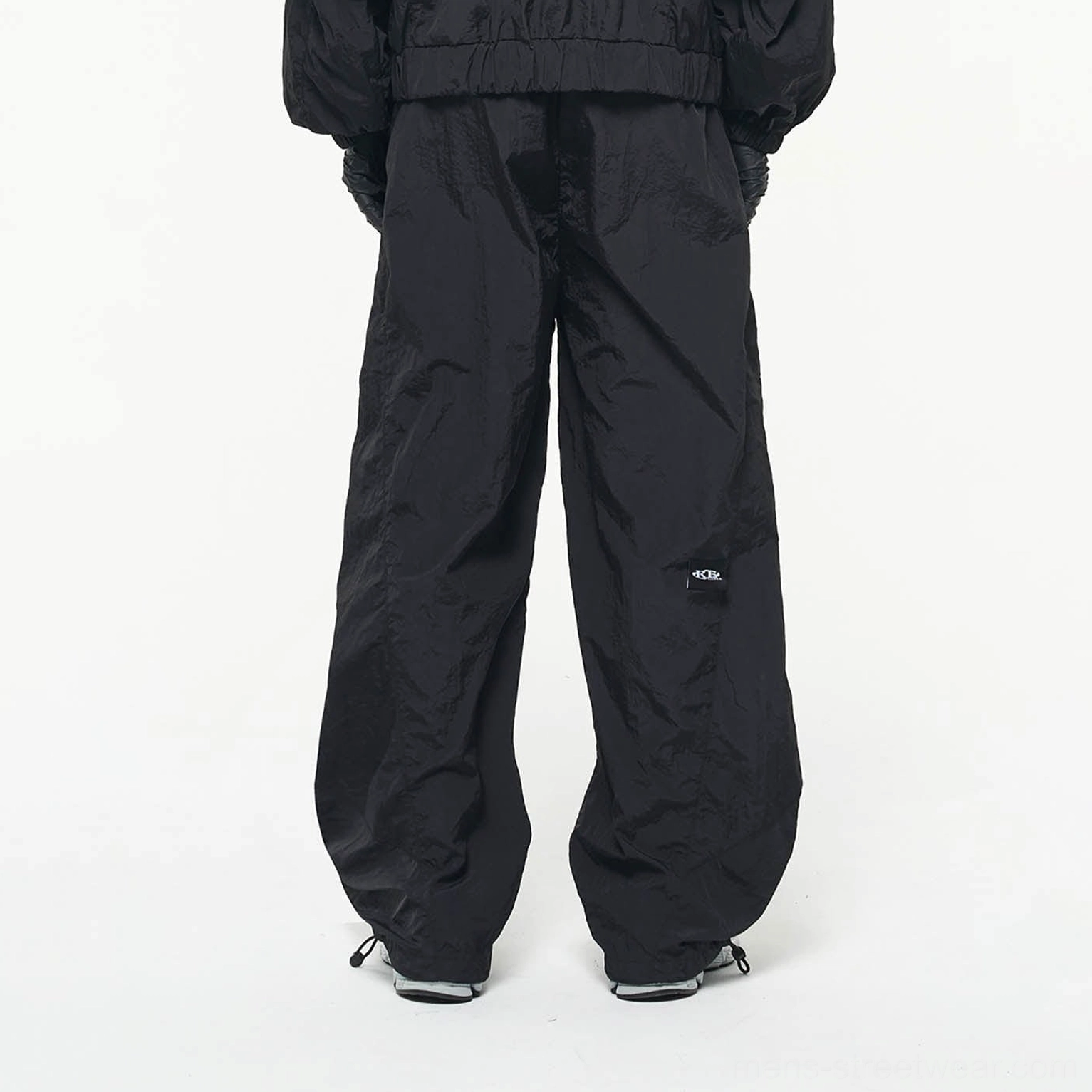 Back view of black crinkled nylon wide-leg track pants with loose silhouette and adjustable ankle drawcords