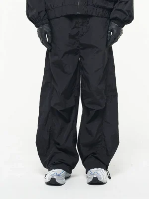 Black crinkled nylon wide-leg track pants front view with adjustable drawstring ankle hems and running sneakers