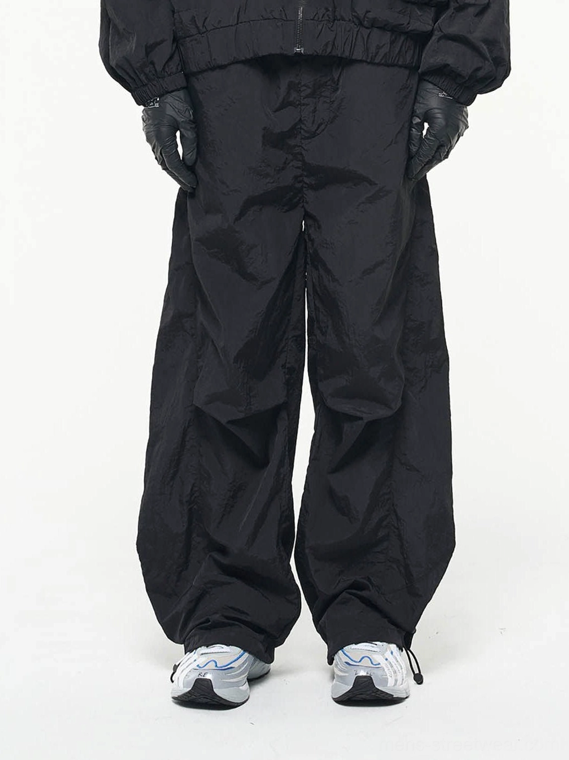 Black crinkled nylon wide-leg track pants front view with adjustable drawstring ankle hems and running sneakers