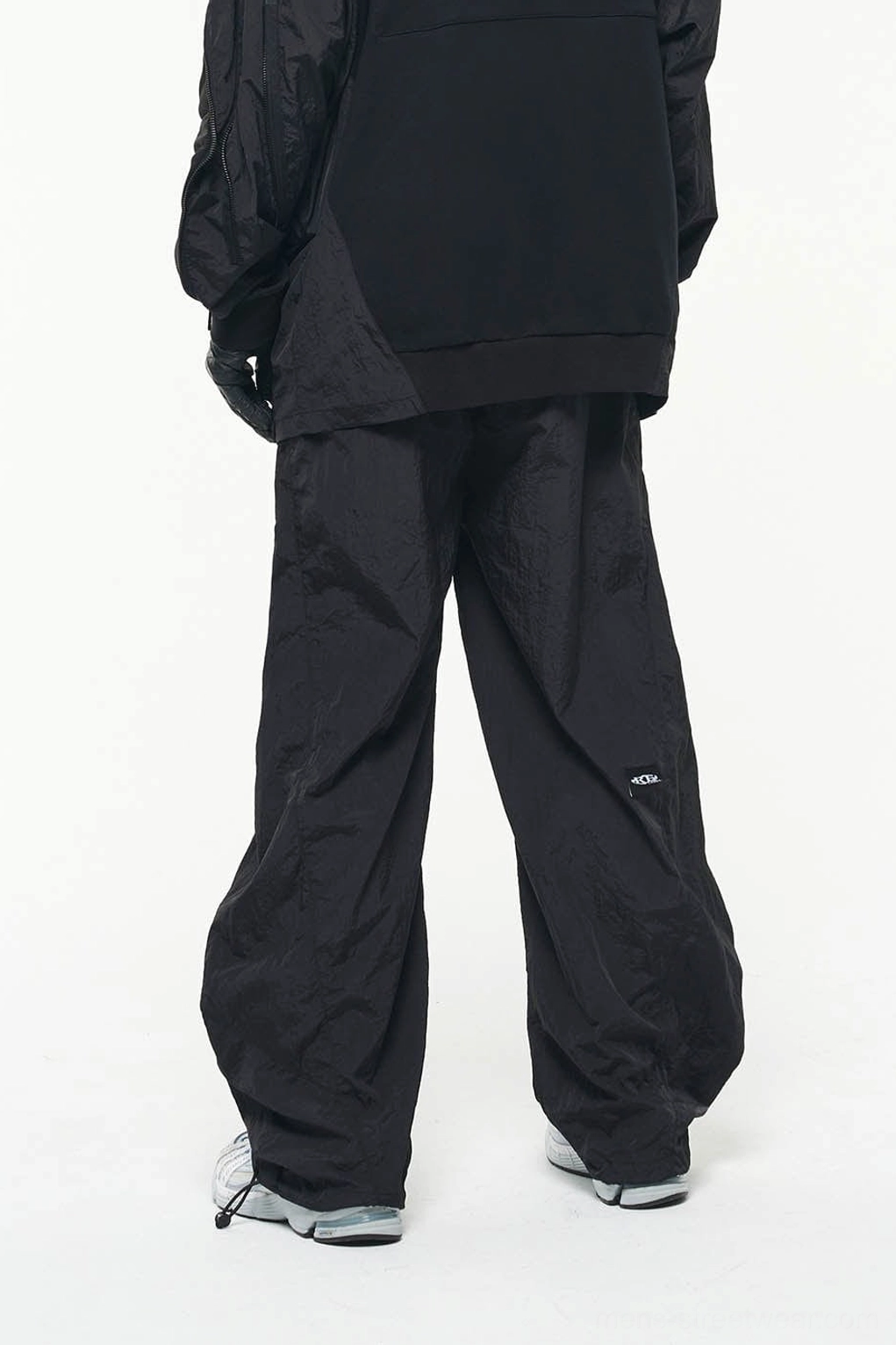 Rear view of black wide-leg nylon track pants with drawstring ankle hems and subtle lower-leg label detail