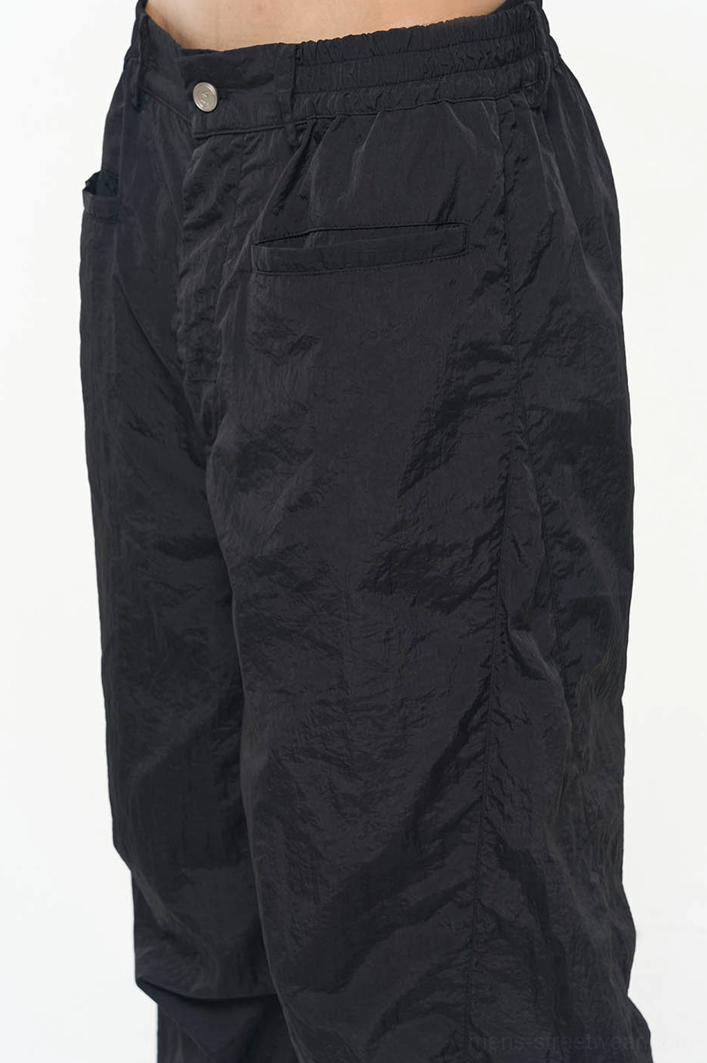 Close-up of black crinkled nylon track pants featuring metal button waist closure and patch back pocket