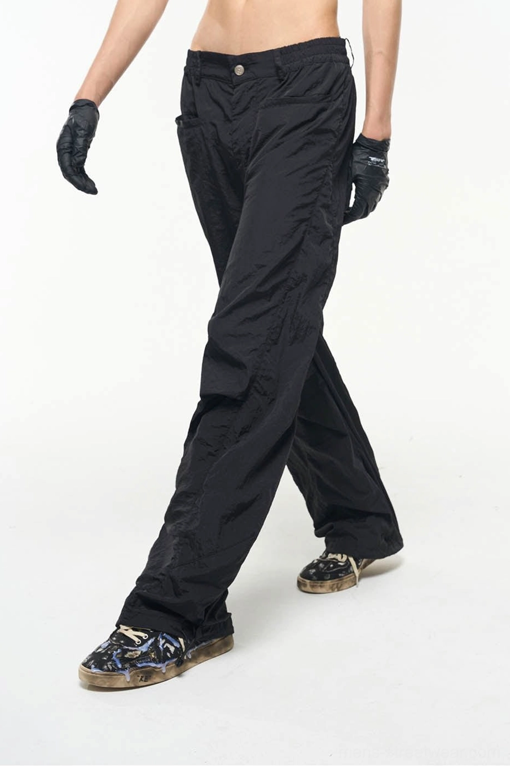 Walking side view of black nylon wide-leg track pants showing loose drape, button waist and crinkled fabric