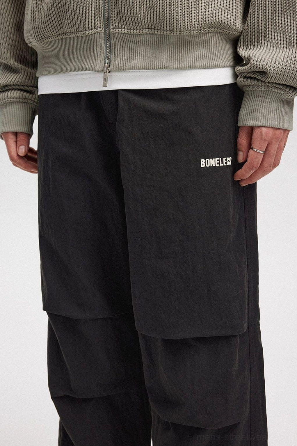 Close-up of black crinkled wide-leg track pants showing front pleats, textured fabric, and waistband detail