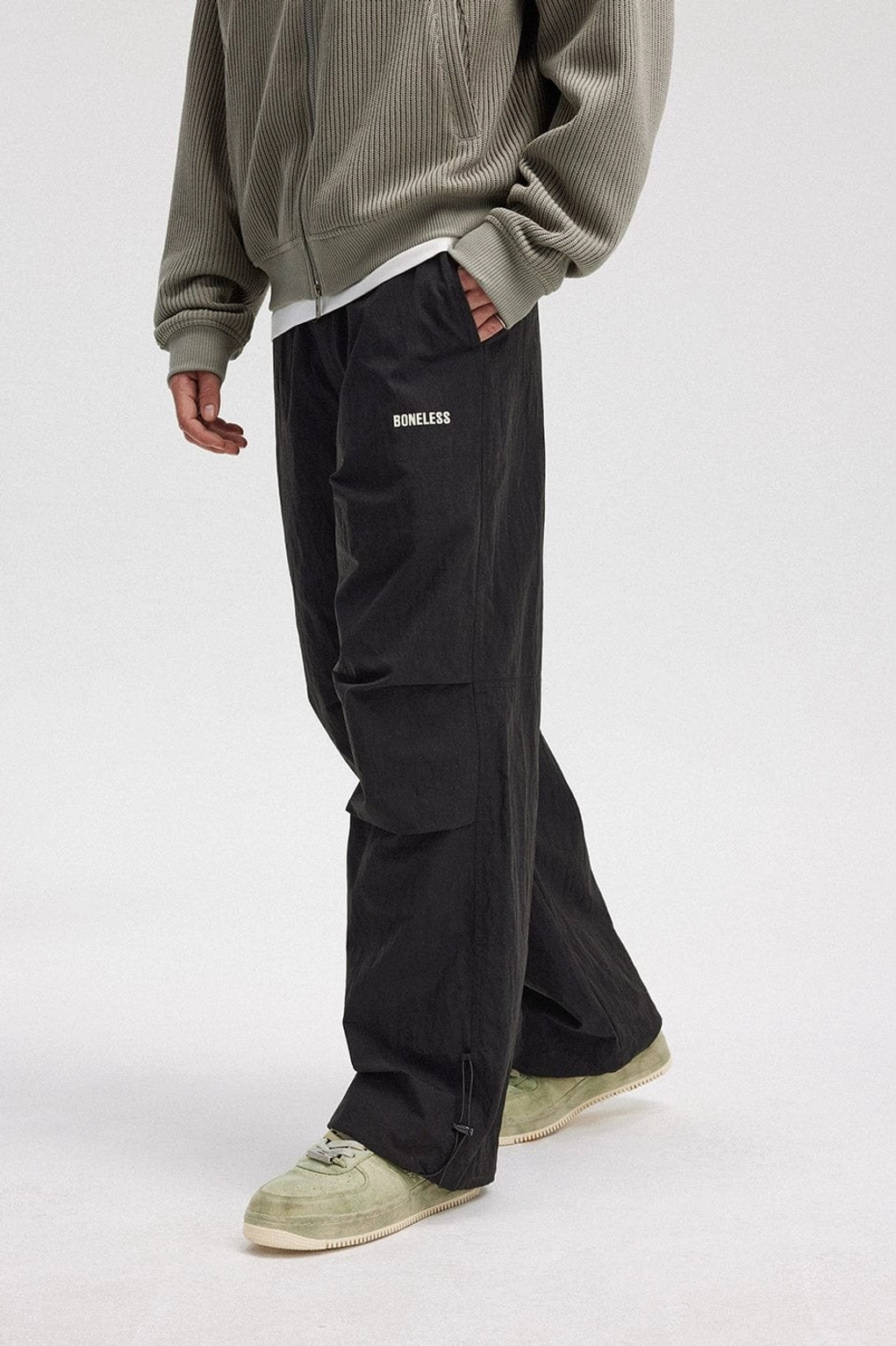 Side view of black crinkled wide-leg track pants with pleated detailing and adjustable ankle drawstrings