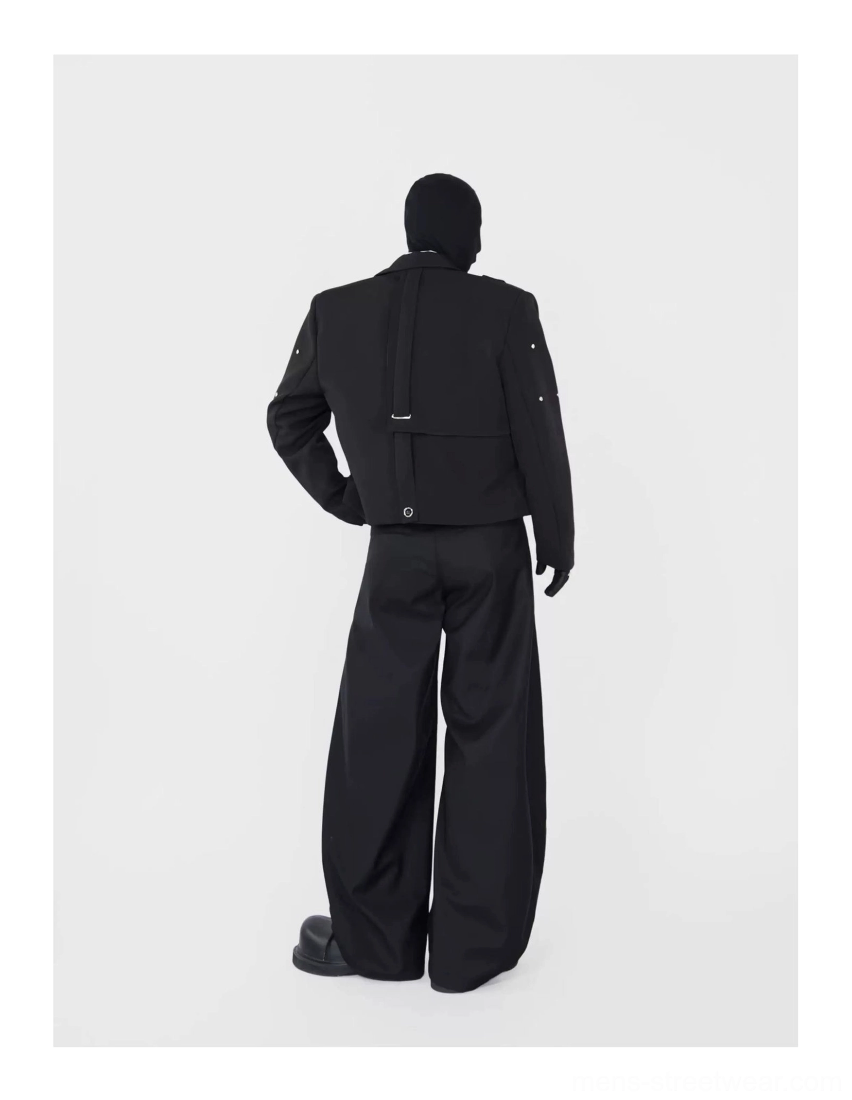 Back view of a black cropped blazer showing back strap detail, exposed seam construction, and structured avant-garde tailoring
