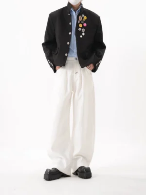 Full front view of black cropped boxy blazer with stand collar flap pockets silver buttons and crest-inspired chest pin cluster
