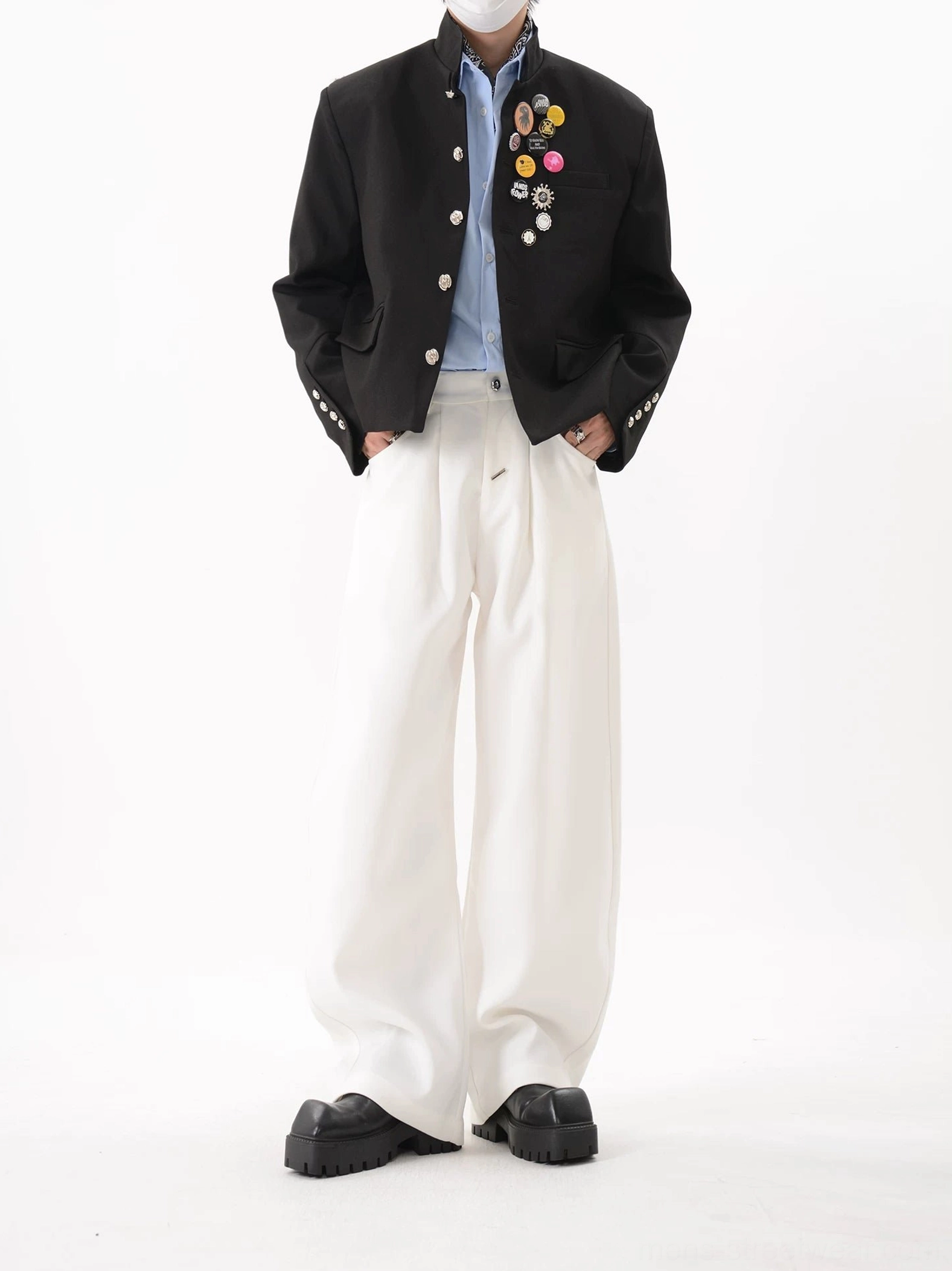 Full front view of black cropped boxy blazer with stand collar flap pockets silver buttons and crest-inspired chest pin cluster