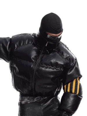 Front close-up of black cropped PU leather puffer jacket with glossy finish, high stand collar, quilted padding, and yellow triple sleeve stripes styled in futuristic techwear streetwear