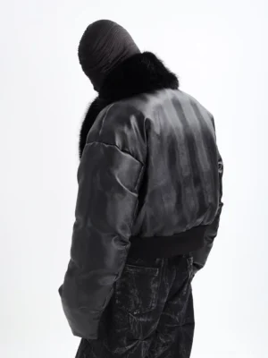 Rear three-quarter view of black cropped puffer jacket showing padded back, ribbed waistband, oversized faux fur collar, and leather-look textured exterior