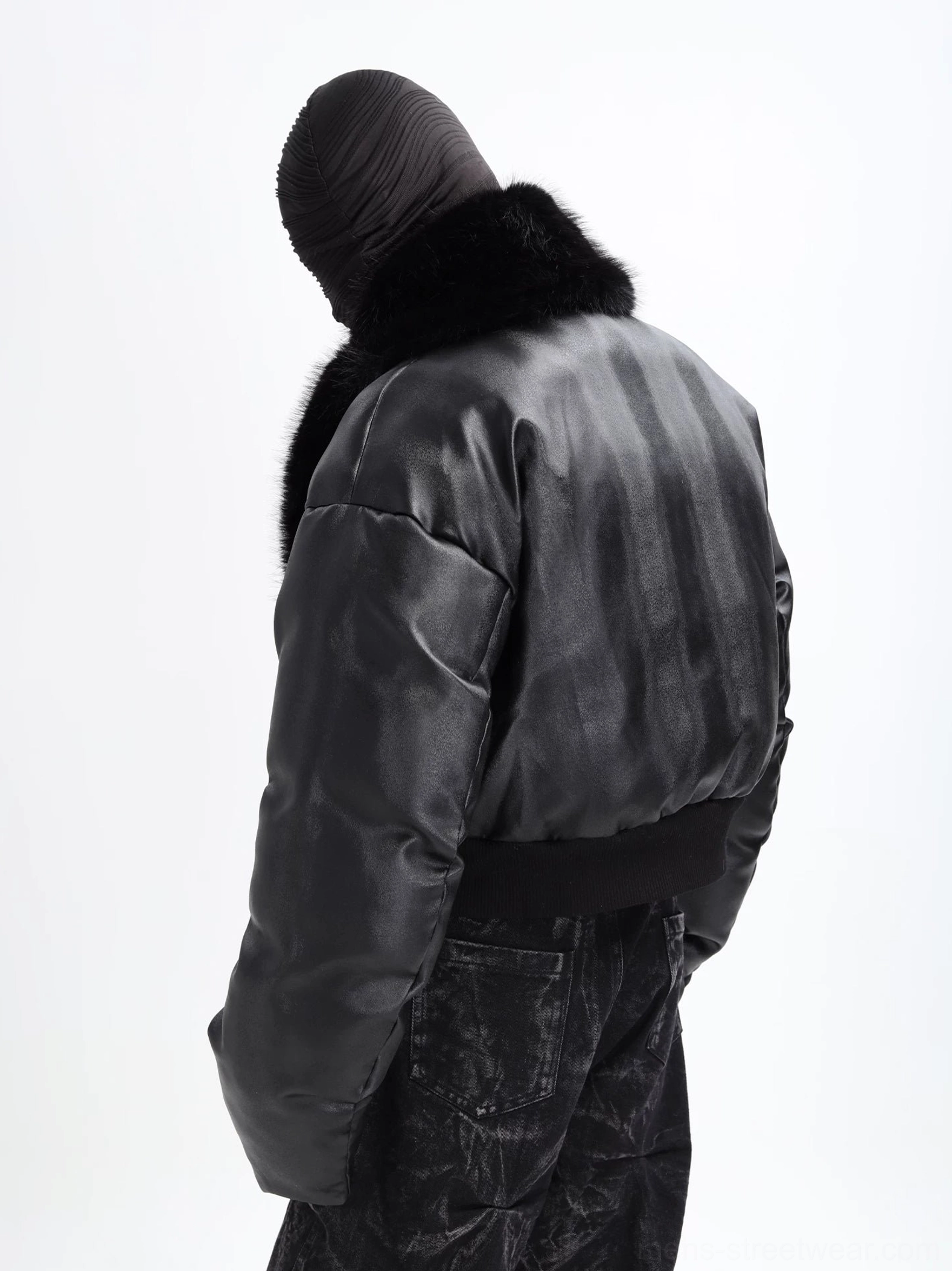 Rear three-quarter view of black cropped puffer jacket showing padded back, ribbed waistband, oversized faux fur collar, and leather-look textured exterior