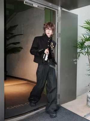 Side view of a black cropped punk blazer styled with wide-leg trousers and a layered metal chain belt in an urban streetwear setting