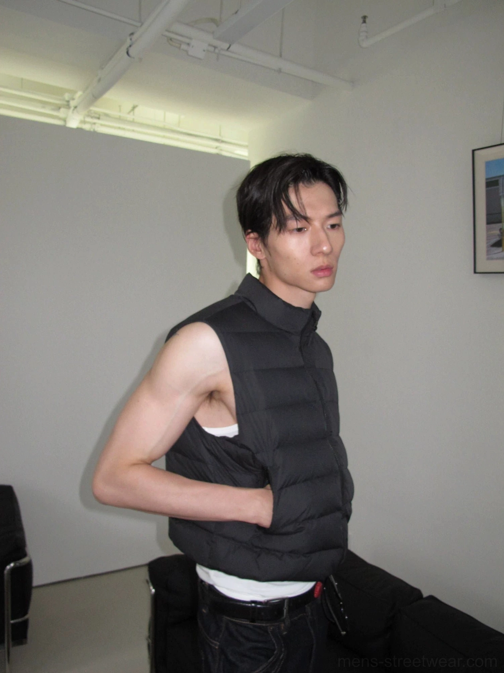 Black cropped quilted puffer vest shown from a seated side view with a visible white inner layer
