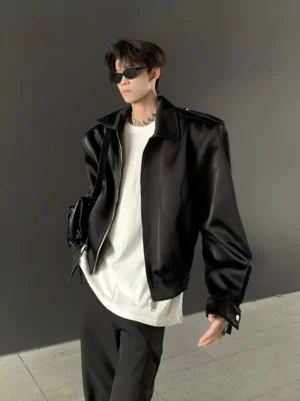 Black cropped structured shoulder bomber jacket worn with sunglasses, silver chain, crossbody bag, and black trousers in a minimalist streetwear outfit