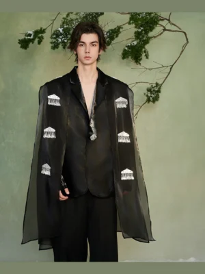 Front full-body view of a black crystal fringe cape blazer with glossy tailored body, sheer asymmetric cape overlay, silver crystal embellishments, and notched lapel