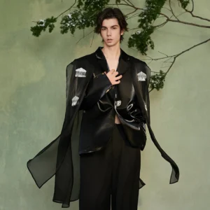 Three-quarter view of a black crystal fringe cape blazer showing the relaxed open fit, glossy finish, flowing sheer cape panel, and decorative crystal fringe