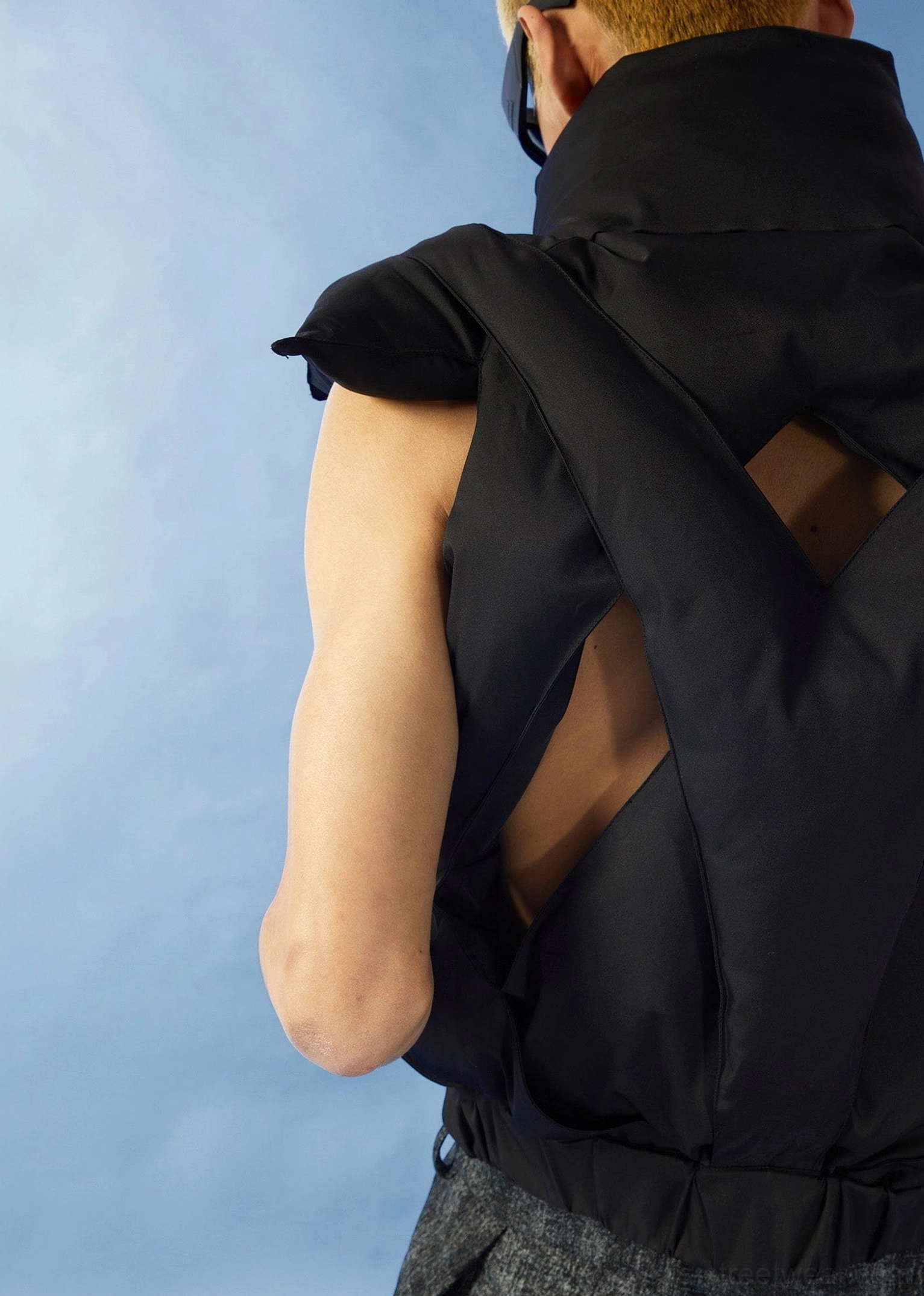 Black cropped puffer vest fashion image highlighting the crisscross cutout back sleeveless construction and quilted panels