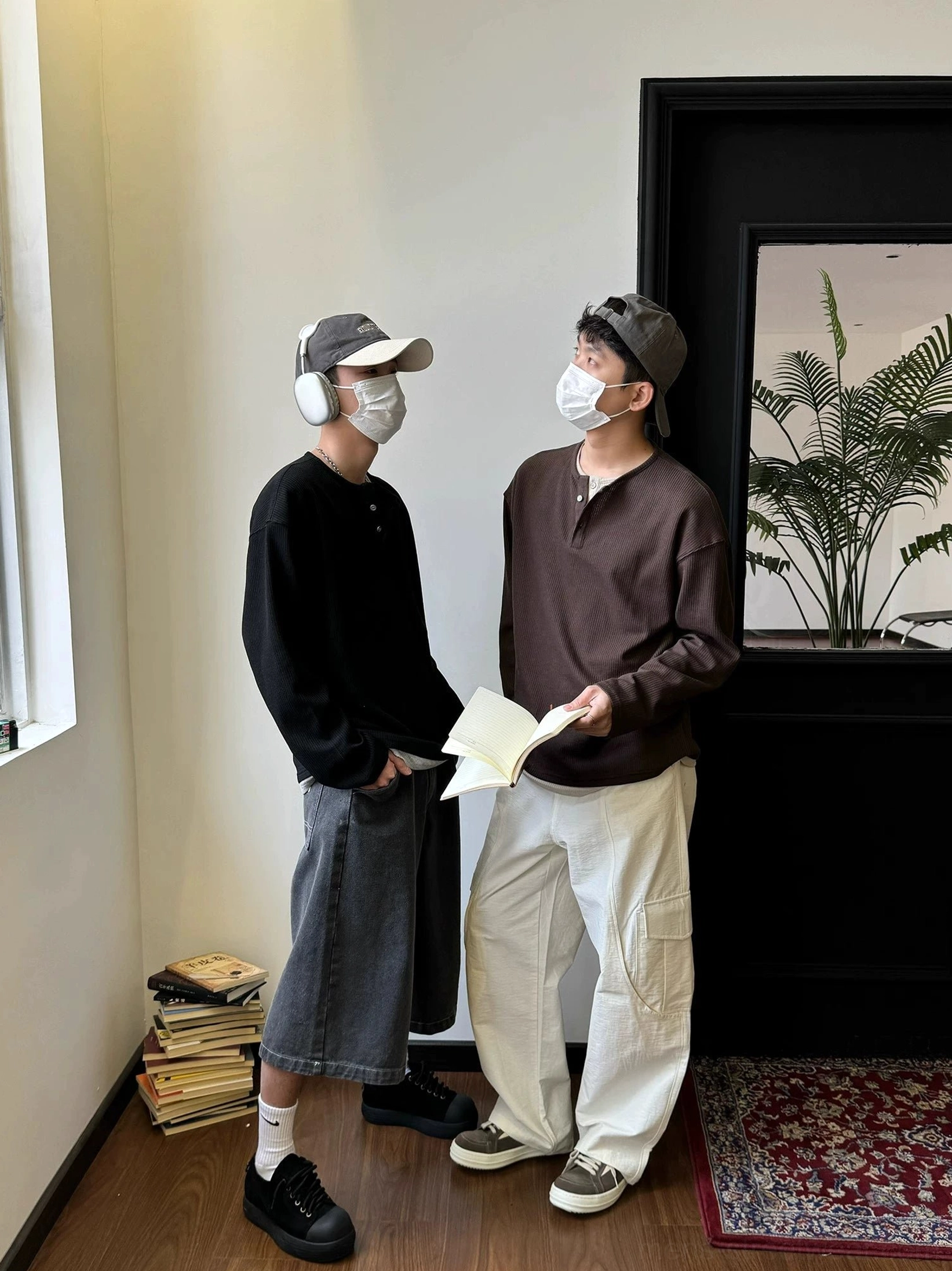 Two male models wearing black and dark brown relaxed Henley shirts with wide-leg trousers and vintage Korean street style