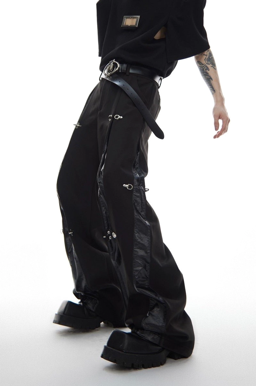 Side view of black deconstructed streetwear trousers featuring asymmetric glossy panels and decorative silver metal clips