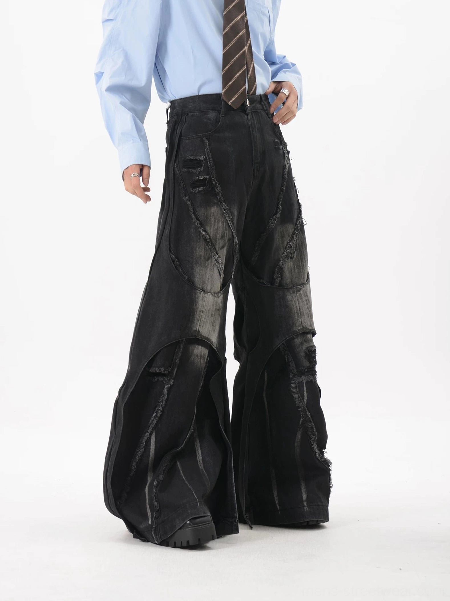 Left front three-quarter view of black deconstructed wide-leg jeans with distressed thigh panels, raw hems, deep pockets, and platform shoe styling
