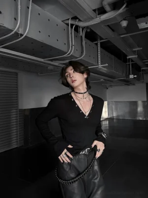 Black deep V ribbed Henley streetwear top with metal neckline detailing on a male model in an industrial underground parking setting