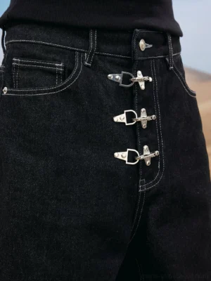 Close-up detail of black denim waist with silver toggle buckles, contrast white stitching, and classic front pockets