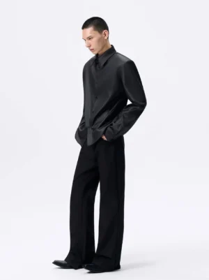 Black detachable shoulder pad glossy cropped shirt in a three-quarter front view, styled with black wide-leg trousers in a minimalist white studio