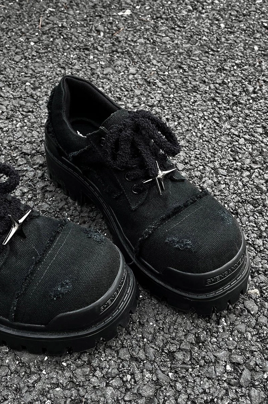 Overhead outdoor view of black distressed canvas platform sneakers on asphalt showing frayed fabric holes and star lace hardware
