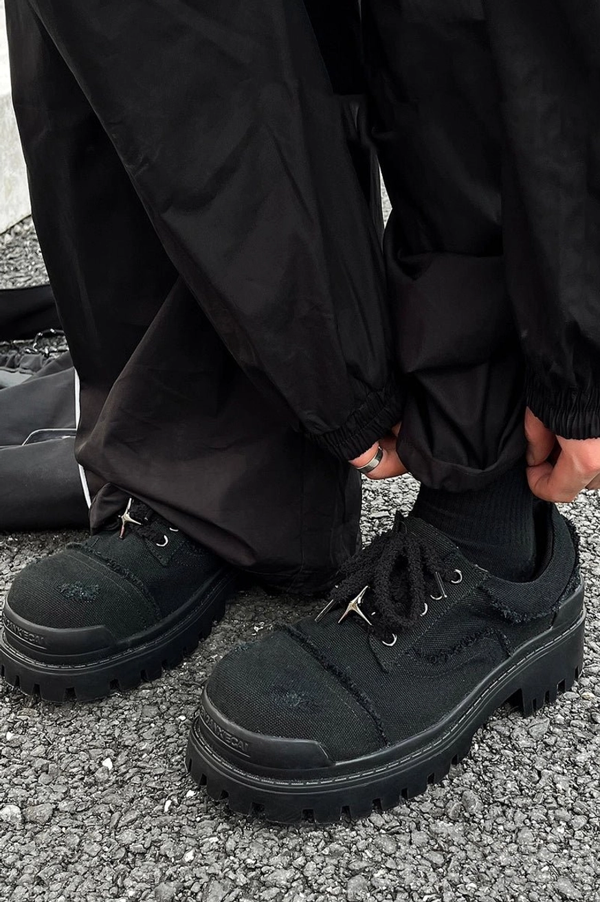 Rear three-quarter streetwear outfit view of black distressed canvas platform sneakers worn with loose black work pants