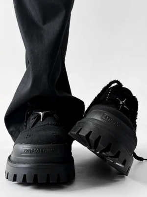 Black distressed canvas platform sneakers with rugged lug soles and silver star lace detail worn with wide leg black pants