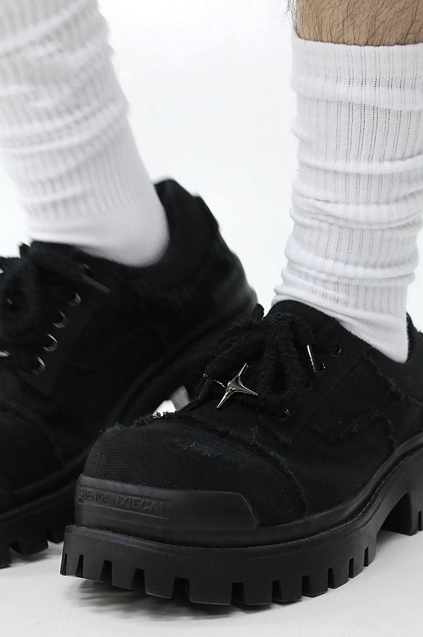Model wearing black distressed canvas platform sneakers with white ribbed socks showing metal star lace decoration and thick sole