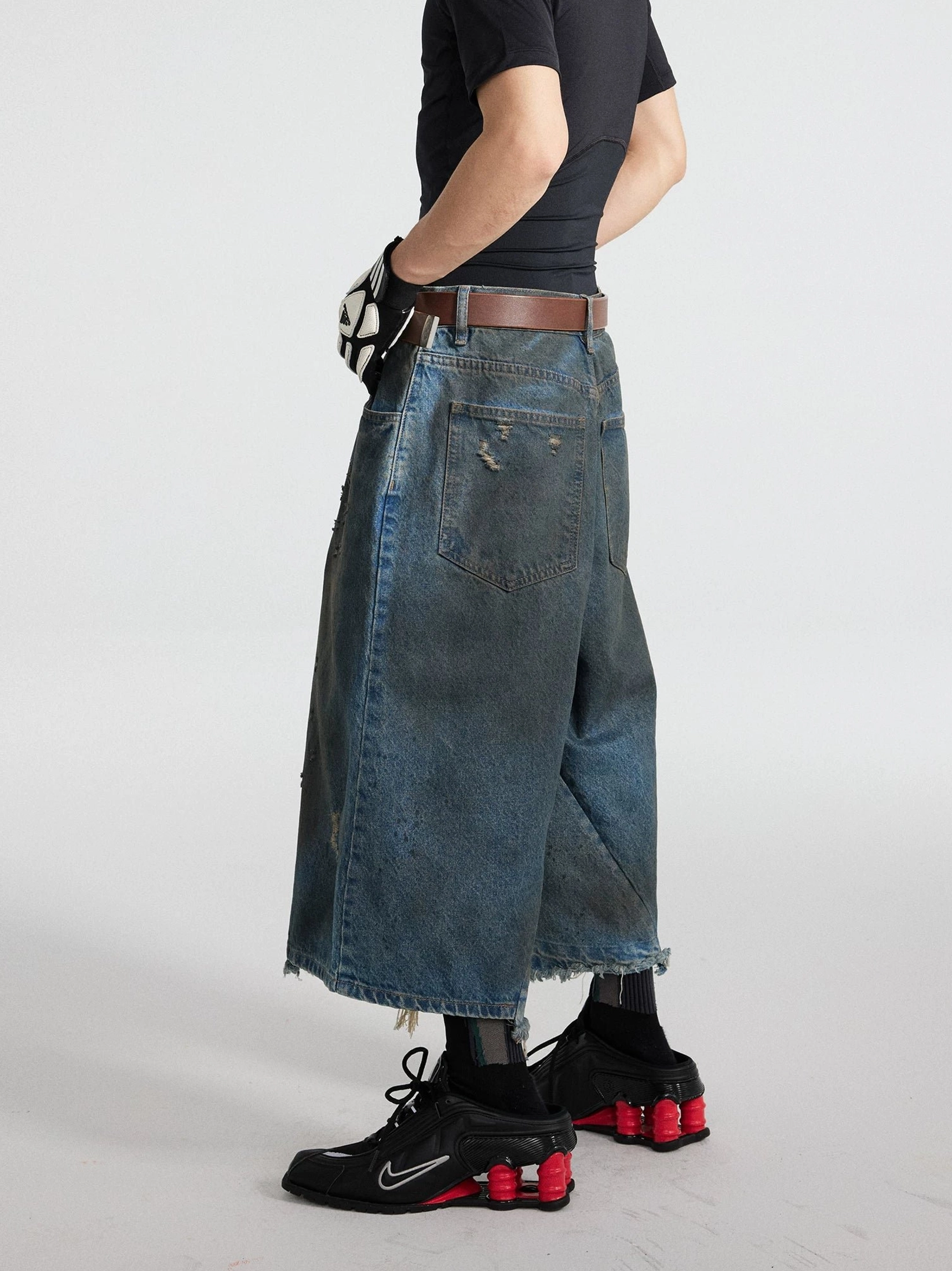 Side full-body view of black distressed cropped denim culottes featuring an extra-wide baggy leg, vintage oil wash, and uneven frayed hems