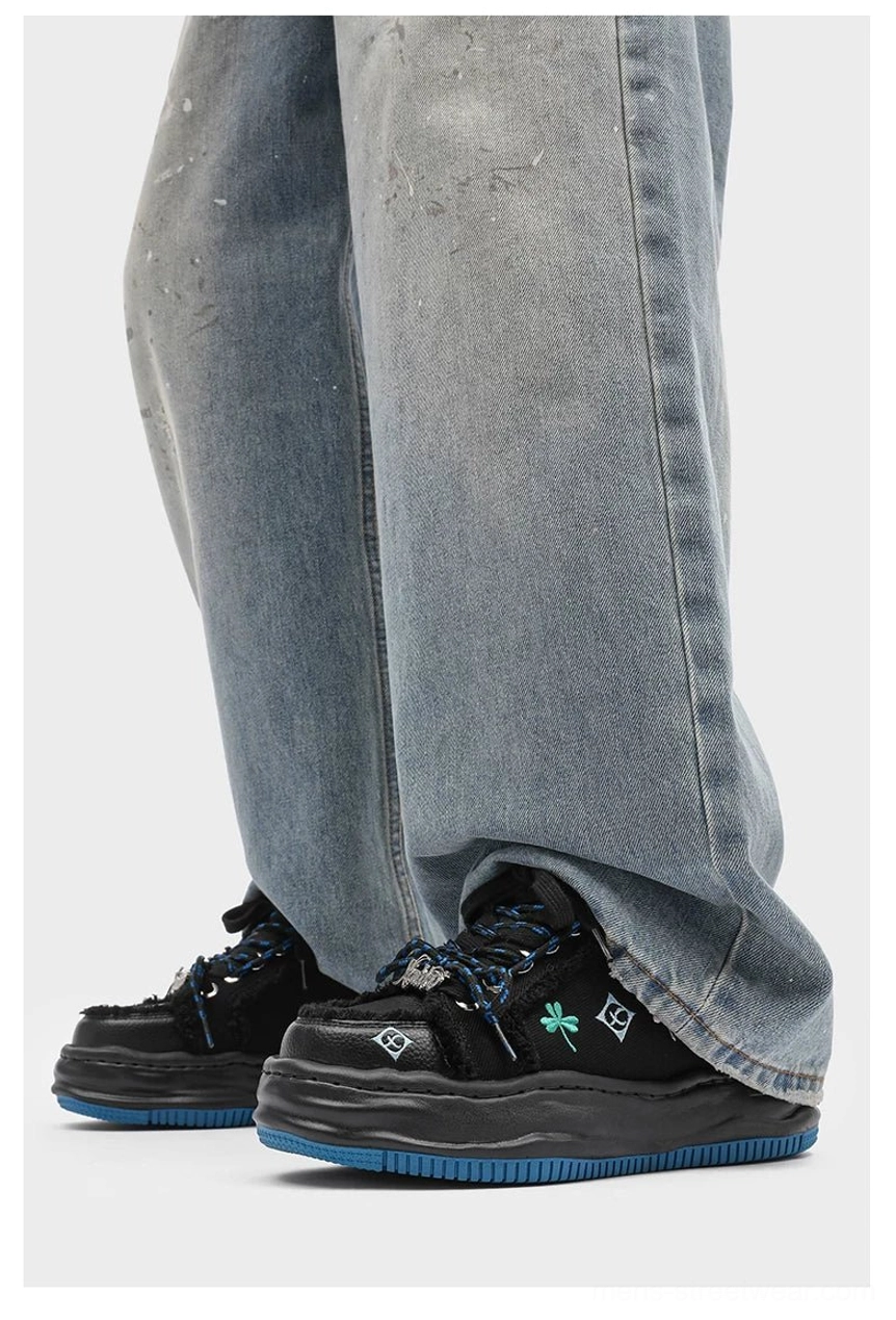 Black distressed embroidered platform sneakers worn with distressed denim showing full elevated sole and streetwear silhouette