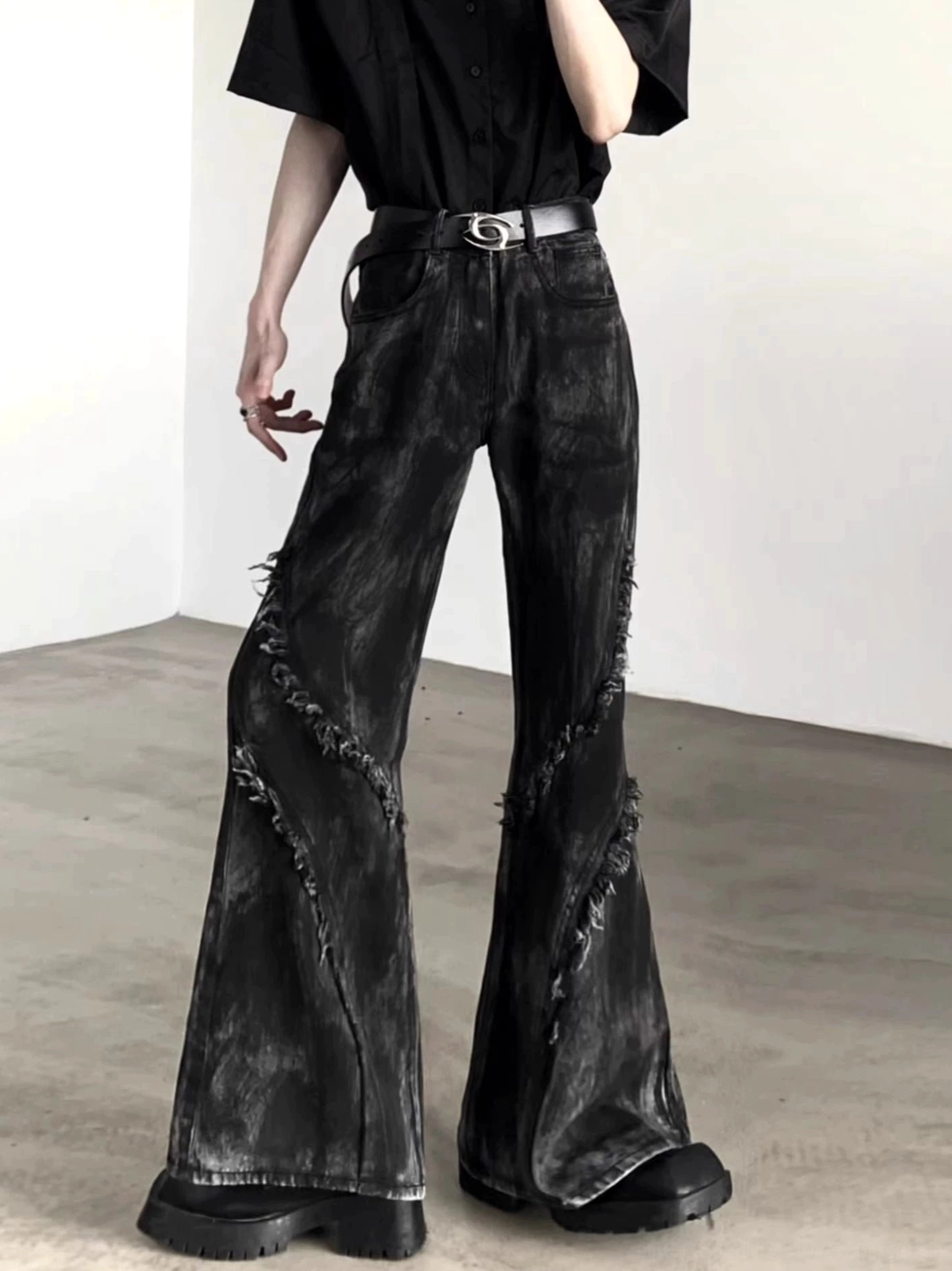 Front three-quarter view of black distressed flared jeans with diagonal frayed seams, washed denim texture, and classic front pockets