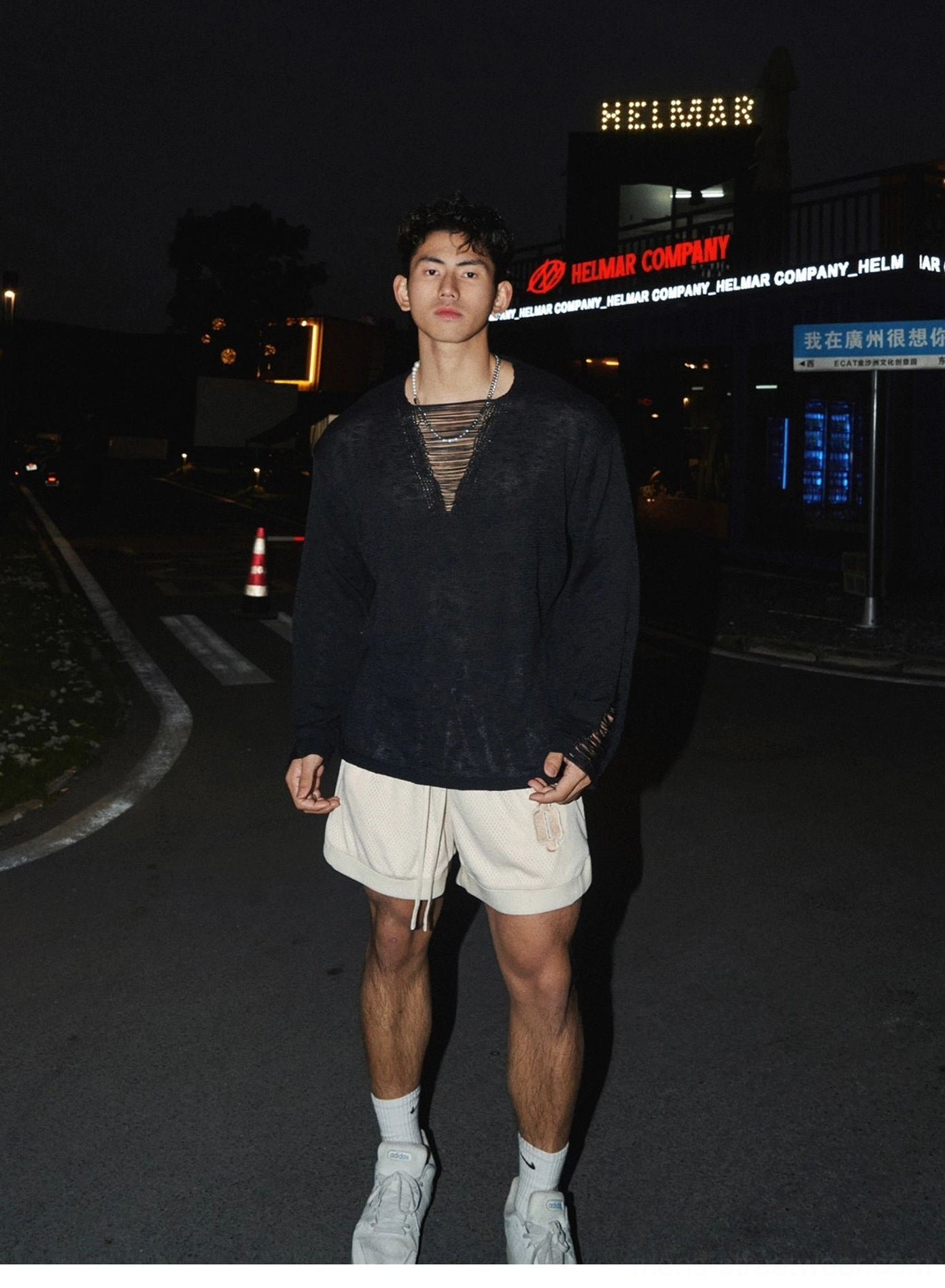 Full-body view of black distressed long sleeve lace-up shirt styled with beige shorts white socks and sneakers