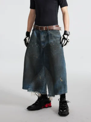 Front full-body view of black distressed oil-washed wide-leg cropped gaucho jeans styled with a fitted black t-shirt, leather belt, gloves, and red black sneakers