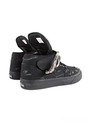 Rear three-quarter view of black punk high-top canvas sneakers showing rubber outsole, distressed upper, wing ankle hardware, and heel detail