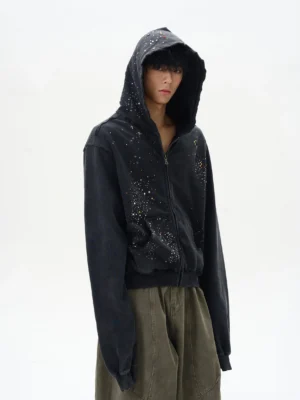 Black distressed rhinestone zip-up hoodie in a left front three-quarter view with faded vintage wash and oversized streetwear fit