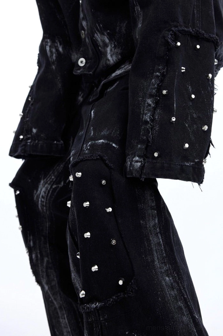 Close-up detail of black distressed cotton denim with metal dome rivets, textured brushed finish, and raw pocket edge