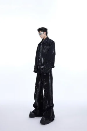Male model wearing black distressed rivet knee wide-leg jeans with brushed white wash and raw flared hems in a white studio