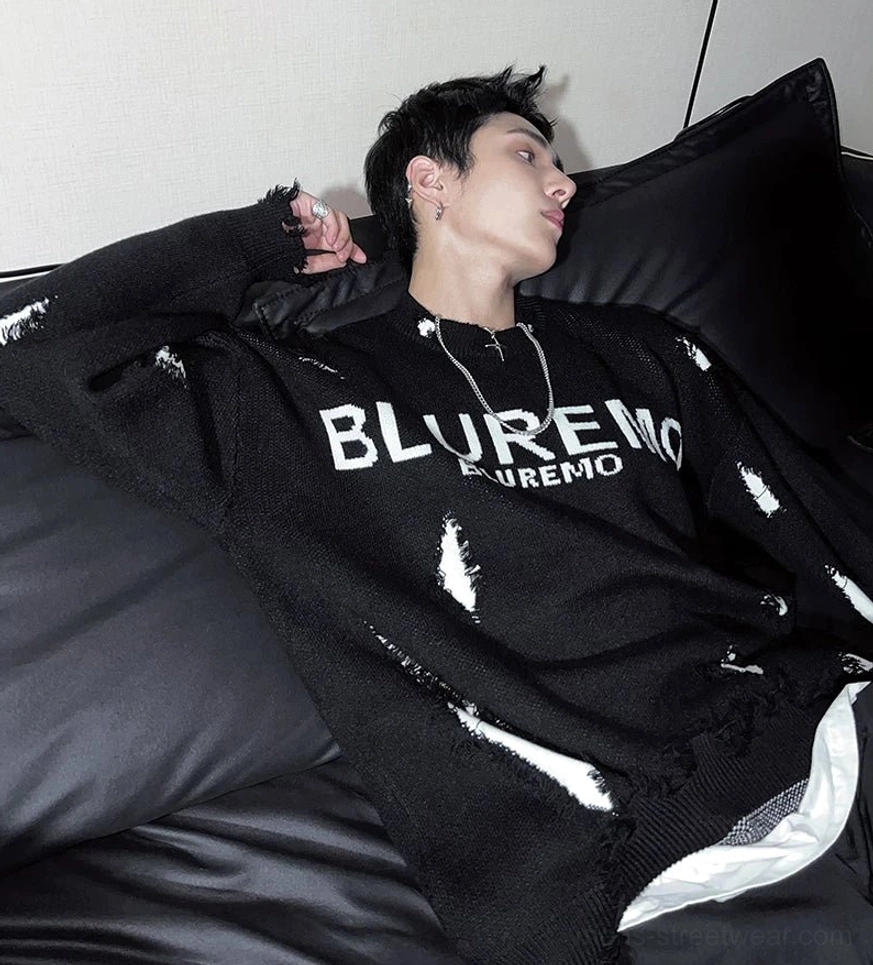 Side profile of a relaxed black distressed knit sweater showing oversized dropped shoulders, scattered shredded accents, and layered streetwear styling