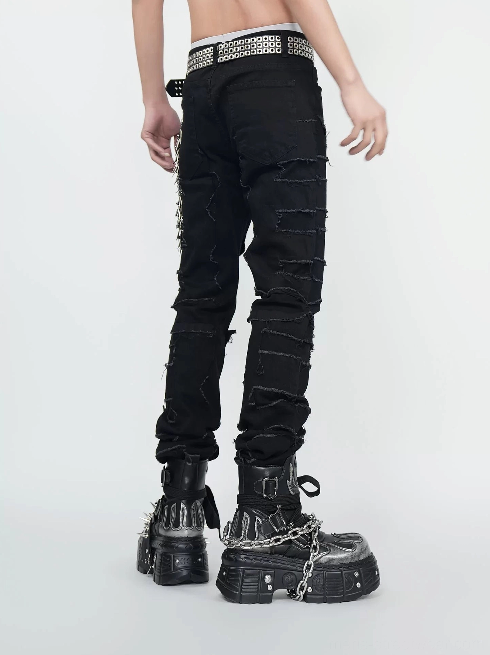 Back view of black distressed stacked-leg jeans with frayed rear denim panels, studded belt, and alternative streetwear design