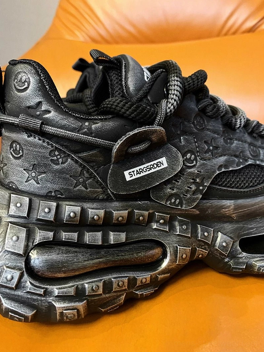 Side close-up of a black distressed chunky streetwear sneaker with padded collar, embossed prints, studded sole details, and textured heel tab