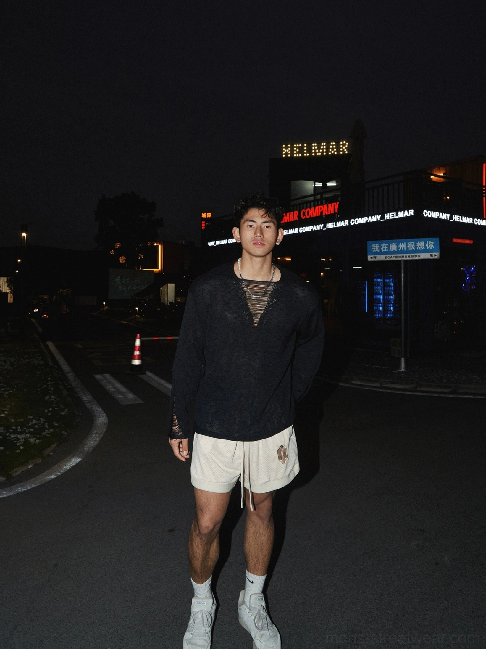 Black distressed V-neck lace-up knit shirt styled with beige shorts and white sneakers in an urban night outfit