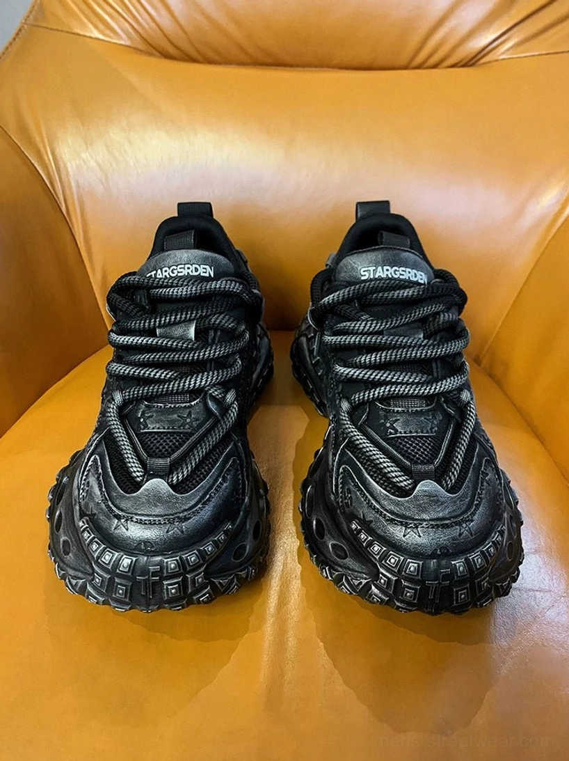 Pair of black distressed chunky streetwear sneakers shown from the front with textured panels, thick rope laces, and sculpted platform soles