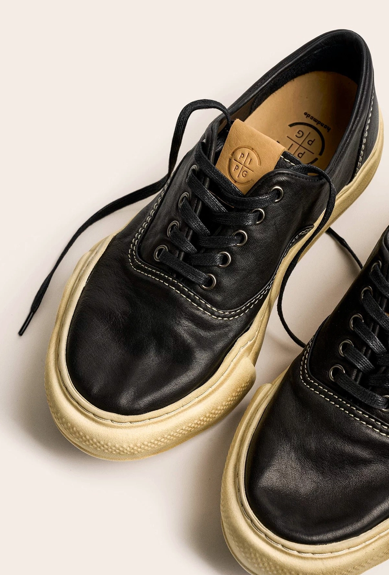 Black distressed washed leather sneakers shown from an oblique front angle with thick aged off-white soles, leather insoles, and classic laces